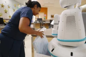 After waving her badge to unlock, a nurse removes a delivered hospital item from a Moxi's storage compartment.Diligent Robotics